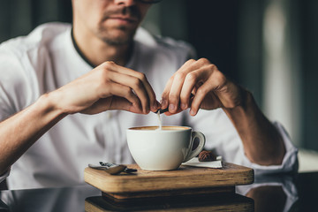 Young man hands holding sugar bag and sweetens coffee in a cafe. selective focus