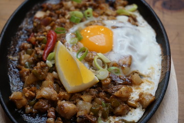 Pork sisig sizzling mince pork Filipino food with raw egg cooking hot on clay pot tray with lemon slice and fresh red chilies Asian cuisine tasty food with pepper on plate 