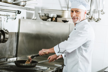 male chef looking at camera while roasting meat steak in restaurant kitchen
