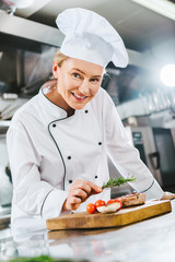 beautiful female chef in uniform decorating meat steak with rosemary in restaurant kitchen