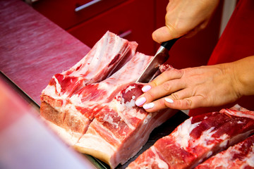 Butcher woman cutting piece of rib meat in her shop with a knife.
