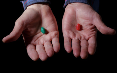 Pills, men's hands on a dark background holding red and green pills, offering a choice