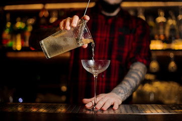 Bartender pouring alcoholic cocktail into a glass