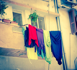Colorful laundry is dried on the balcony of the old building with stucco wall.  Aged photo.