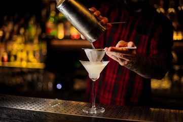 Mixologist pouring fresh and sour drink into a cocktail glass