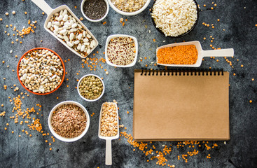 Cereals and legumes in the range. Peas, beans, lentils, rice, quinoa, chia seeds, oatmeal, in small cups and scoops on a dark stone background, culinary background, background about products