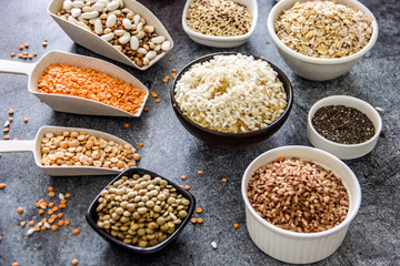 Cereals and legumes in the range. Peas, beans, lentils, rice, quinoa, chia seeds, oatmeal, in small cups and scoops on a dark stone background, culinary background, background about products