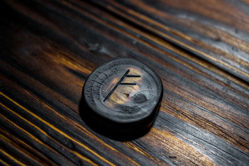 Rune Fehu carved from wood on a wooden background - Elder Futhark