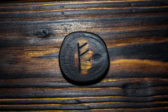 Rune Fehu carved from wood on a wooden background - Elder Futhark