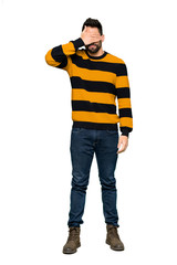 Naklejka premium Full-length shot of Handsome man with striped sweater covering eyes by hands. Do not want to see something on isolated white background