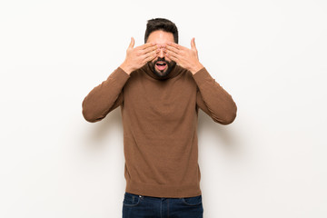 Handsome man over white wall covering eyes by hands. Surprised to see what is ahead