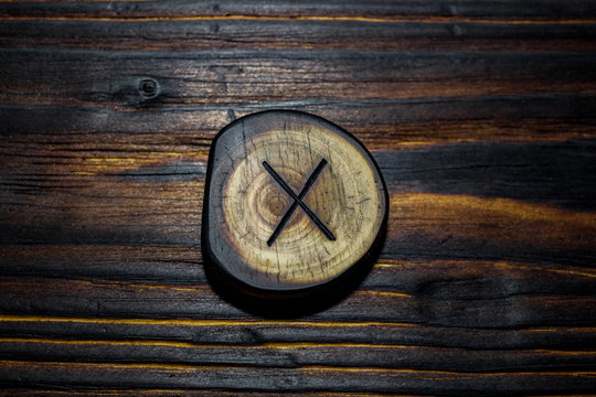 Rune Gyfu (Gebo) carved from wood on a wooden background - Elder Futhark