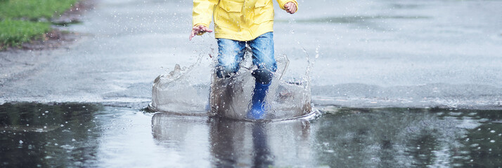 A wet child is jumping in a puddle. Fun on the street. Tempering in summer