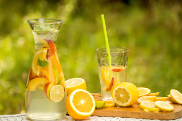 A carafe and a glass with an illuminating summer drink  lemonade and various fruits against the...