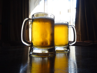 Two full mugs of light beer on the table at pub
