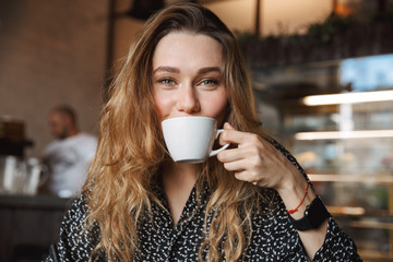 Beautiful young pretty woman sitting in cafe indoors drinking coffee.