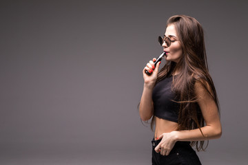 Close-up Portrait of sexy young woman with suglasses smoking vape isolated on gray background. Vapor concept. Vaping e-Cigarette.