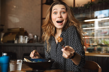 Excited beautiful young pretty woman sitting in cafe indoors have a breakfast.