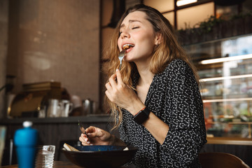 Excited beautiful young pretty woman sitting in cafe indoors have a breakfast.