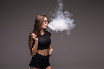 Young pretty woman in sunglasses and black clothes vaping and blowing smoke of electronic cigarette...