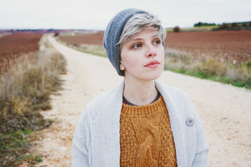 Woman with short and gray hair is alone in the beggining of a rural path in a cold autumn day