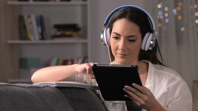Serious student e-learning using tablet and notebook sitting on a couch in the night at home