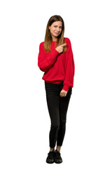 A full-length shot of a Young woman with red sweater pointing to the side to present a product over isolated white background