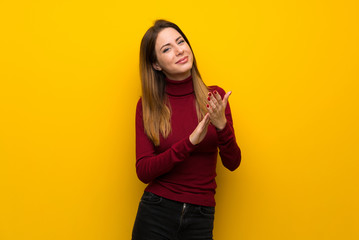 Woman with turtleneck over yellow wall applauding after presentation in a conference