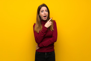 Woman with turtleneck over yellow wall surprised and pointing side