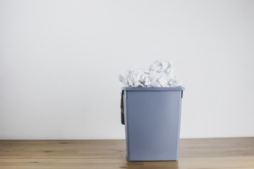 A trash can to the top filled with crumpled paper