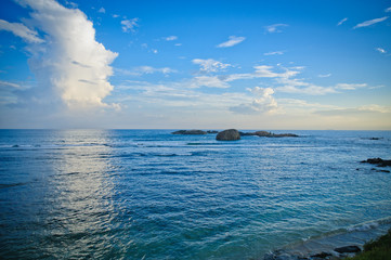 Fototapeta premium Ocean and blue sky with clouds. Rocks in the water.