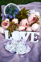 Word love, bouquet of pink peony flowers and two hearts on purple background outdoors, copy space. Selective focus. Valentine Day, love or wedding day concept