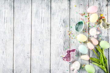 Easter background with colorful pastel eggs and tulip flowers, wooden background top view copy space