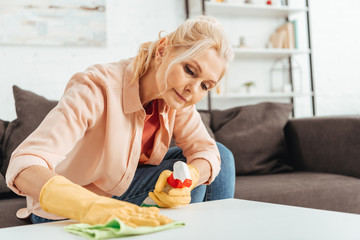 Concentrated senior woman in rubber gloves cleaning table