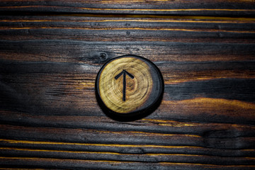 Rune Tiwaz (Tyr) carved from wood on a wooden background - Elder Futhark