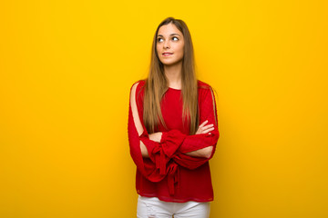 Young girl with red dress over yellow wall with confuse face expression while bites lip