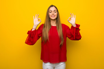 Young girl with red dress over yellow wall in zen pose