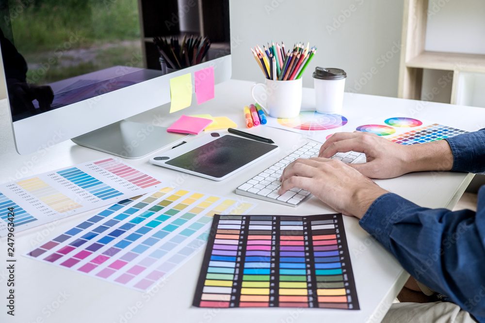 Poster Image of male creative graphic designer working on color selection and drawing on graphics tablet at workplace with work tools and accessories
