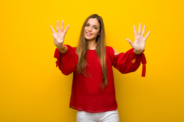 Young girl with red dress over yellow wall counting nine with fingers