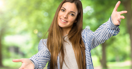 Young girl with striped shirt presenting and inviting to come with hand at outdoors