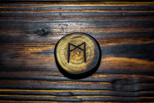 Rune Mannaz (Mann) carved from wood on a wooden background - Elder Futhark