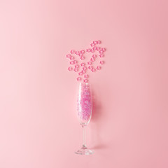 Champagne glass with pink glitter on pastel pink background. Minimal party drink style.