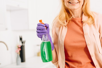 Cropped view of smiling senior woman in rubber glove holding spray