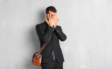 Businessman with beard covering eyes by hands and looking through the fingers