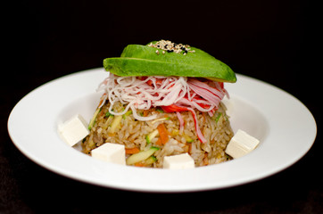 Yakimeshi fried rice with avocado and surimi presented in white plate against a dark backgound.