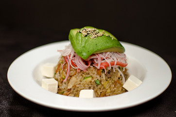 Yakimeshi fried rice with avocado and surimi presented in white plate against a dark backgound.