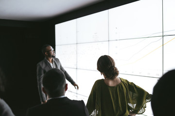 Black african businesswoman giving a presentation at a business conference. Large video screen with...