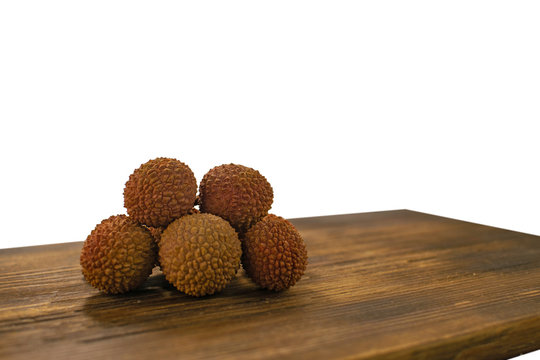Fresh lychee and peeled showing the red skin and white flesh with green leaf on a wooden background. Lychi with leaves - tropical fruit.