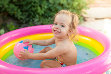 Children playing in inflatable baby pool. Kids swim and splash in colorful garden play center. Happy little girl playing with water toys on hot summer day. Family having fun outdoors in the backyard.