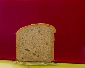 Section of loaf of white loaf close up prepared in the bread machine on the openwork chromeplated support on a red background.